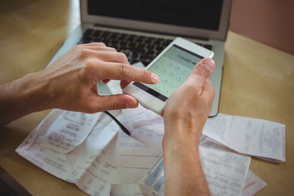 Mid section of man calculating bills on mobile phone-3